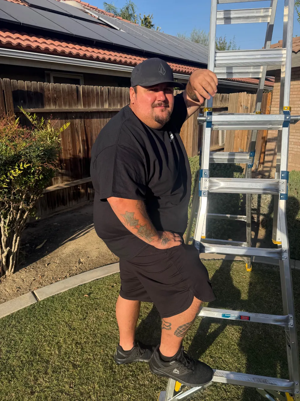 Roman from Suds and Studs standing on a ladder step beside a home with solar panels